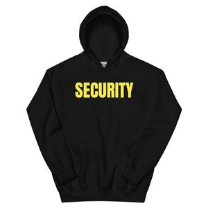 Könnte beinhalten: Schwarzer Kapuzenpullover mit dem Wort "SECURITY" in gelben Blockbuchstaben auf der Brust. Der Pullover hat eine Vordertasche und eine Kapuze mit Kordelzug. Ein lässiges Kleidungsstück für Sicherheitspersonal.