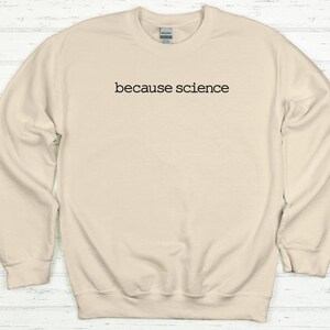May include: Cream-colored sweatshirt with the phrase "because science" printed in black, centered on the chest. The long-sleeved crewneck top is made of a soft material and has a ribbed collar, cuffs, and hem.