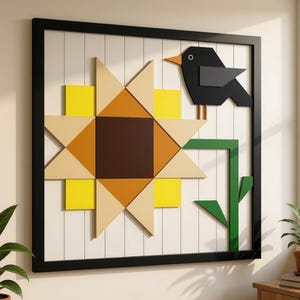 May include: A square wall art piece in a black frame featuring a geometric sunflower design with yellow, tan, and brown triangles. A stylised black bird with an orange beak is perched on the flower stem, set against a white vertical panelled background.