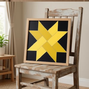 May include: A square framed wall art piece featuring a geometric eight-pointed star design. The star is composed of interlocking yellow rectangular segments set against a solid black background, enclosed within a light-toned wooden frame.