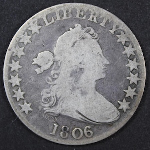 May include: A silver coin from 1806 featuring a profile of a woman's head, surrounded by stars and the word "LIBERTY". The coin has a worn appearance, with visible details of the design.