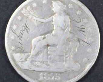 May include: A silver coin featuring a seated female figure holding a sprig. The coin is inscribed with "May 12" and the year "1875". The coin has a detailed design with stars around the edge and the initials "J.M."