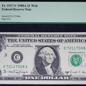 May include: A one-dollar Federal Reserve Note from 1988, featuring George Washington. The note is graded as Gem New 65PPQ. The text "THE UNITED STATES OF AMERICA" is visible, along with the serial number C72117508A.