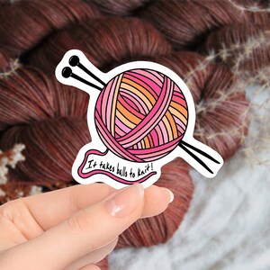 May include: A sticker featuring a colorful ball of yarn with knitting needles. The yarn is in shades of pink, orange, and yellow. The text "It takes balls to knit!" is written on the sticker.