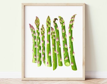 May include: A framed print featuring a watercolor illustration of several asparagus spears. The asparagus stalks are a vibrant green with pink and purple accents. The artwork is set against a white background and framed in light wood.