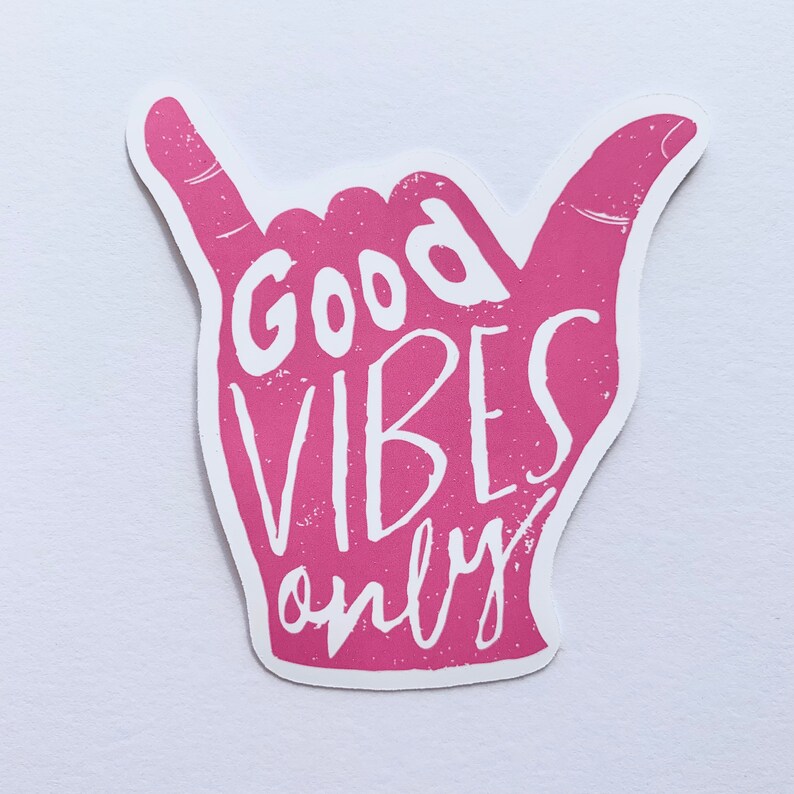 May include: A pink sticker in the shape of a hand making the shaka sign. The words "Good Vibes Only" are printed in white, with a distressed texture. The sticker is on a white background.