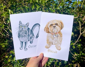 May include: Two white rectangular art prints featuring detailed illustrations of pets. The left print shows a grey cat with yellow eyes and the name Oscar. The right print shows a light brown, fluffy dog with a pink collar and the name Biscuit.