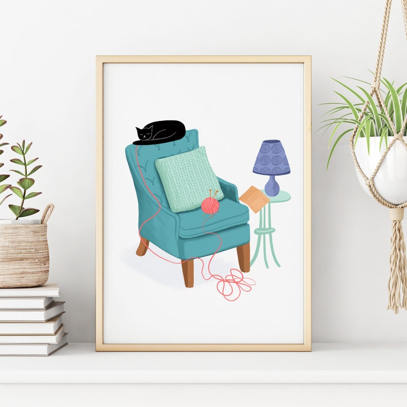 May include: A teal armchair with a black cat sleeping on the back, a knitted throw pillow, and a pink ball of yarn. A blue lamp with a white shade sits on a small table next to the chair.