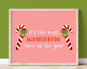 May include: A framed print with a pink background and the text "It's the most WONDERFUL time of the year." Two candy canes with red and white stripes and green bows flank the text. The frame is light brown.