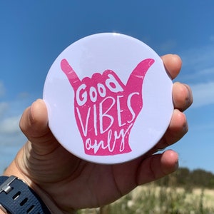 May include: White round sticker with a pink hand giving the shaka sign. The hand has the text "Good Vibes Only" written on it.