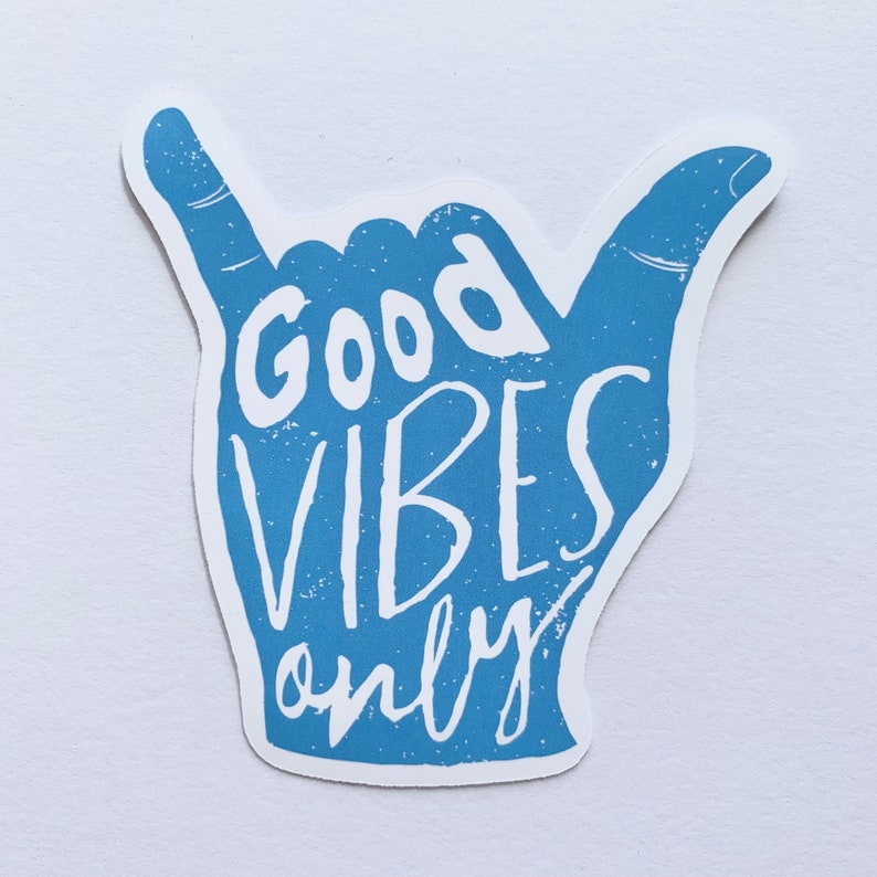 May include: A blue sticker in the shape of a hand gesture, with the words "Good Vibes Only" in white lettering. The sticker has a distressed, textured appearance, and is set against a white background.