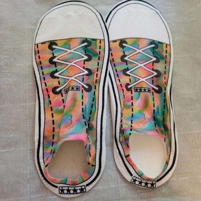May include: A pair of white socks with a colorful tie-dye design that looks like a pair of sneakers. The socks have black laces and a white sole.