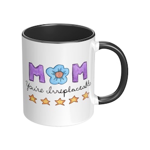 May include: White ceramic mug with a black interior and handle. The mug features the word "MOM" in purple letters with a blue flower in the center. Below the word "MOM" is the phrase "You're irreplaceable" and five gold stars.