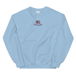 May include: Light blue sweatshirt with a small embroidered Puerto Rican flag and the text "Puerto Rico Isla del Encanto".