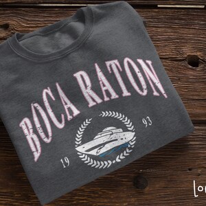 May include: A dark gray sweatshirt with a white graphic print of a boat and the text "Boca Raton 19 93" in pink.