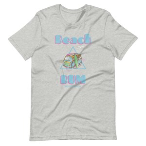 May include: A light gray t-shirt with a blue and pink graphic of a vintage van with a surfboard on top. The text "Beach Bum" is above the van and "Myrtle Beach" is below the van.