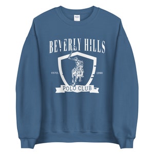 May include: A blue sweatshirt with a white graphic of a polo player on a horse, a shield, and the text "Beverly Hills Polo Club" with "Estd. 1990".