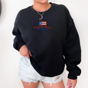 May include: Black sweatshirt with a Puerto Rico flag and the text "Puerto Rico Isla del Encanto" embroidered on the front.
