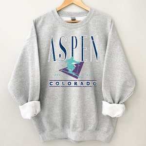 May include: Gray sweatshirt with a vintage-style graphic of a skier on a mountain with the text "Aspen Colorado" and "Est. 1964" printed on it.