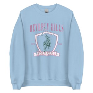 May include: Light blue sweatshirt with a vintage-style graphic of a polo player on a horse. The graphic includes the text "Beverly Hills Polo Club" and the years "Est. 1990".
