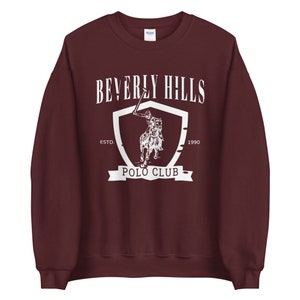 May include: Burgundy sweatshirt with a white graphic of a polo player on a horse, a shield, and the text "Beverly Hills Polo Club Est. 1990"