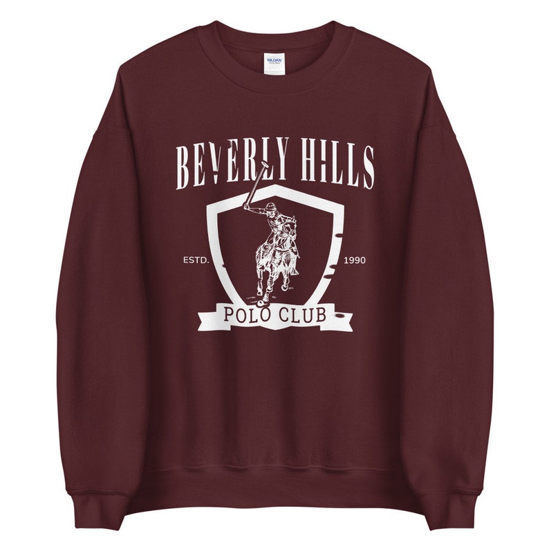 May include: Burgundy sweatshirt with a white graphic of a polo player on a horse, a shield, and the text "Beverly Hills Polo Club Est. 1990"