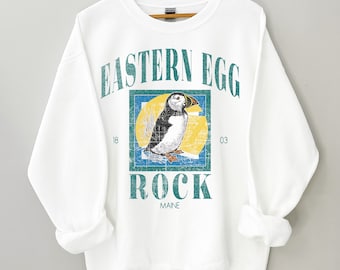 May include: White sweatshirt with a vintage-style graphic of a puffin in a blue and yellow frame. The text "Eastern Egg Rock Maine" is printed on the sweatshirt.