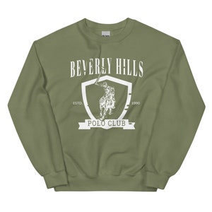 May include: A green sweatshirt with a white graphic of a polo player on a horse inside a shield. The text "Beverly Hills Polo Club" is written below the shield. The text "Est. 1990" is written above the shield.