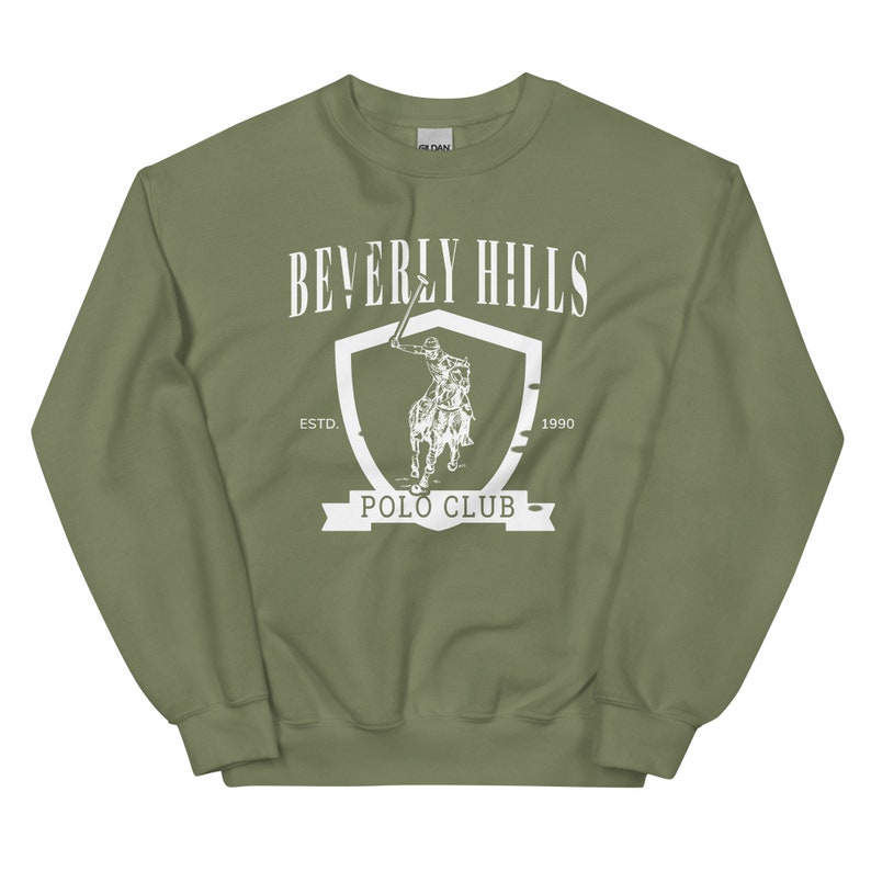 May include: A green sweatshirt with a white graphic of a polo player on a horse inside a shield. The text "Beverly Hills Polo Club" is written below the shield. The text "Est. 1990" is written above the shield.
