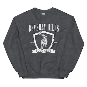 May include: A dark gray sweatshirt with a white graphic of a shield with a polo player riding a horse. The shield has the text "Beverly Hills Polo Club" and "Est. 1990".