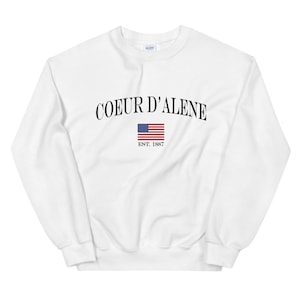 May include: White sweatshirt with black text that reads "COEUR D'ALENE EST. 1887" and a small American flag.