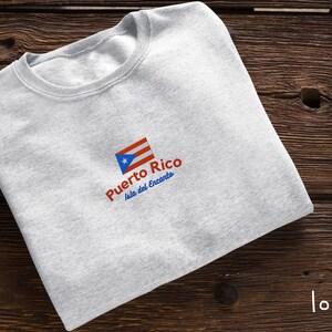 May include: A gray t-shirt with a red, white, and blue Puerto Rican flag design. The text "Puerto Rico Isla del Encanto" is printed below the flag.