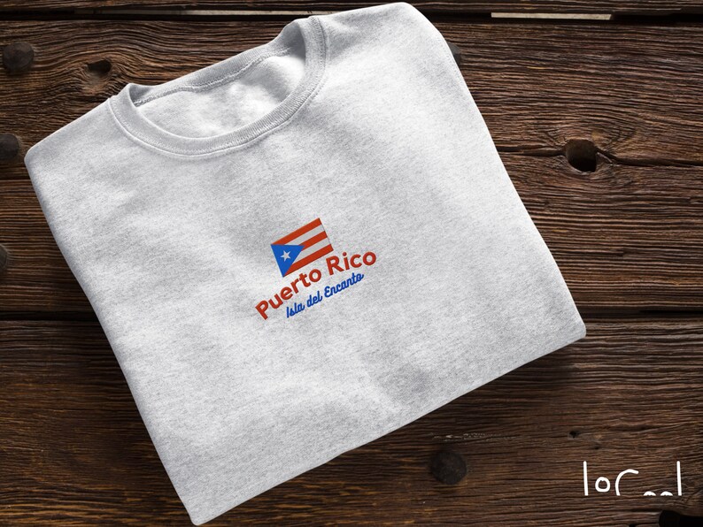 May include: A gray t-shirt with a red, white, and blue Puerto Rican flag design. The text "Puerto Rico Isla del Encanto" is printed below the flag.