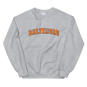 May include: A gray sweatshirt with the word "BALTIMORE" printed in orange on the front.