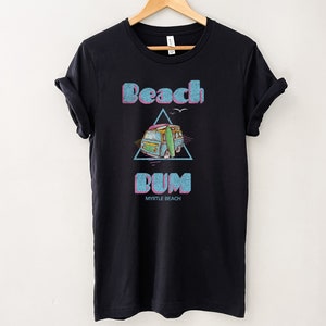 May include: Black t-shirt with a graphic of a blue van with a surfboard on top, inside a pink triangle. The text "Beach Bum" is above the van and "Myrtle Beach" is below the van.