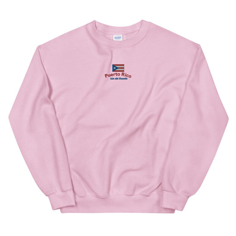 May include: Pink crewneck sweatshirt with a small embroidered Puerto Rican flag and the text "Puerto Rico, Isla del Encanto".