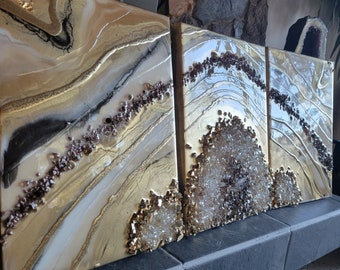 Könnte beinhalten: Drei abstrakte Kunstleinwände in einem Farbschema aus Gold, Weiß und Braun. Die Leinwände zeigen ein geschichtetes, fließendes Design mit einem Hauch von Glanz.