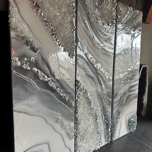 May include: A three-panel abstract art piece with a white and gray background. The panels feature a swirling, agate-like design with silver glitter embedded in the resin.