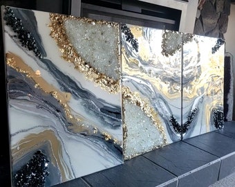 May include: A set of three abstract paintings with a white, gray, and gold color scheme. The paintings feature a swirling, marbled design with black and white glitter accents.