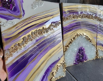 Puede incluir: Tres pinturas abstractas sobre lienzo con un esquema de color morado, blanco y dorado. Las pinturas presentan un diseño de remolino y mármol con toques de brillo.