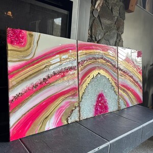 May include: A three-piece abstract art set featuring pink, white, and gold resin with embedded crystals. The artwork is displayed on a stone surface.