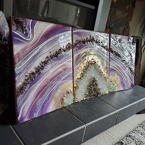 May include: A three-panel abstract artwork with a geode design. The panels feature swirling patterns in shades of purple, white, and gold, accented with silver lines and embedded crystals. The artwork is displayed on a dark surface.