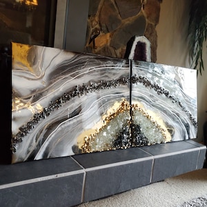 May include: Two abstract art pieces in a black, white and gold colour scheme. The pieces are made of resin and feature a geode-like design with black and white swirls and a gold accent.
