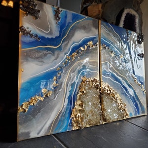 May include: Two abstract resin art panels with blue, white, and gold accents. The panels feature a swirling, agate-like design with gold leaf accents and a crystal-like texture.