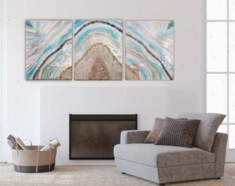 May include: A three-piece abstract art print set featuring a blue, white, and gold agate design. The prints are framed and hung on a white wall above a fireplace.
