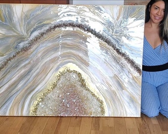 May include: A large abstract painting with a white, gray, and gold color scheme. The painting features a large, white, and gold agate geode with a sparkly, glittery texture. The geode is surrounded by swirling, abstract lines in shades of gray and gold.