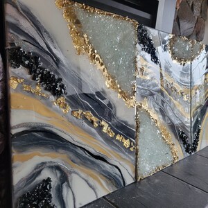 May include: Three abstract resin art panels with black, white, gold, and clear glitter accents. The panels feature a flowing, marbled design with gold leaf accents and clear crystals.