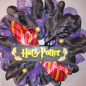 May include: A decorative wreath featuring a Harry Potter theme. The wreath is made of purple and black mesh, with a red and gold striped tie, black glasses, and a wooden sign that says "Harry Potter" in yellow.