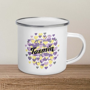 May include: White enamel mug with a silver rim and handle. The mug features a design of purple, yellow, and gray hearts with the name "Tasmin" in black cursive lettering.