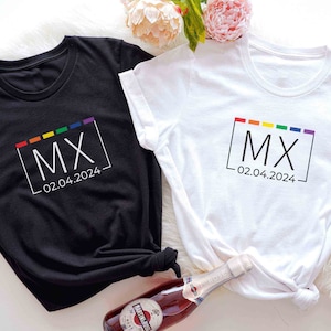 Puede incluir: Dos camisetas, una negra y una blanca, con una caja de colores arcoíris que contiene las letras "MX" y la fecha "02.04.2024" impresas en ellas.